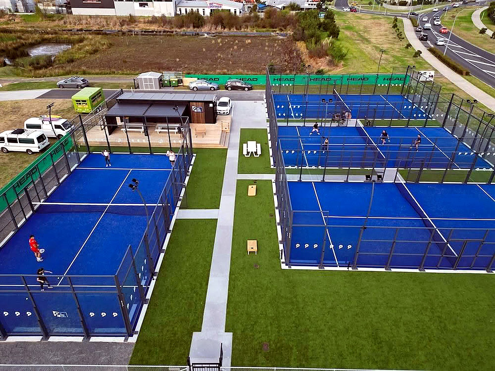 Légifelvétel egy kültéri padel klubról: öt kék műfüves panoráma pálya, moduláris recepció és közösségi tér
