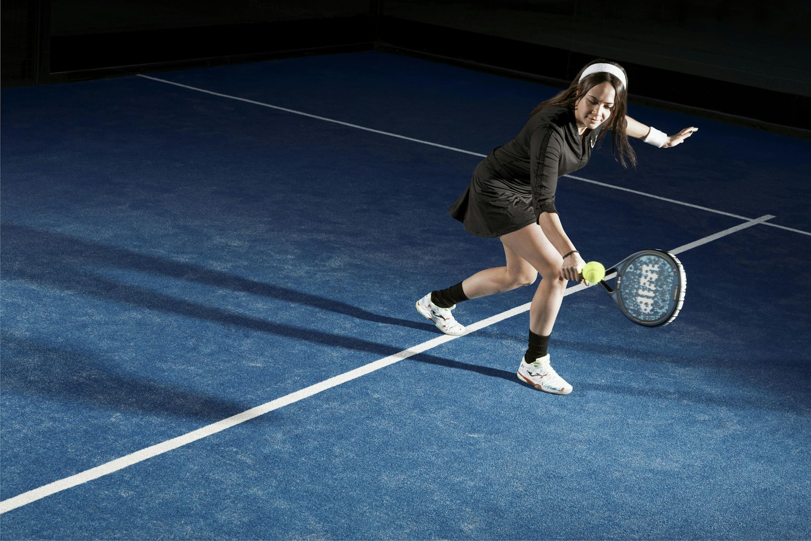 Padel játékos lendületes ütése kék műfüves pályán, esti világításban